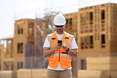 Photo for Worker man on the building construction. Worker using phone, builder chatting on phone a break from work. Architect with mobile phone. Construction site worker outdoor portrait - Royalty Free Image