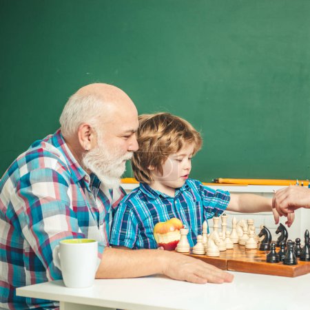 Téléchargez les photos : Grandfather and grandson playing chess. Grandpa teaching grangson at chess school - en image libre de droit