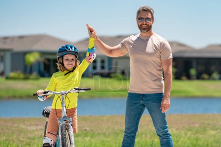 Photo for Happy Fathers day. Father support son. Father and son in a helmet riding bike. Little cute adorable caucasian boy in safety helmet riding bike with father. Family outdoors summer activities - Royalty Free Image