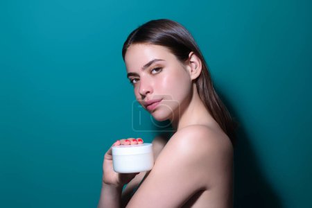 Téléchargez les photos : Young woman applying body cream against studio background. Beauty routine. Studio face of a beautiful woman with perfect skin. Wrinkle cream. Concept of beauty. Woman applying face cream - en image libre de droit