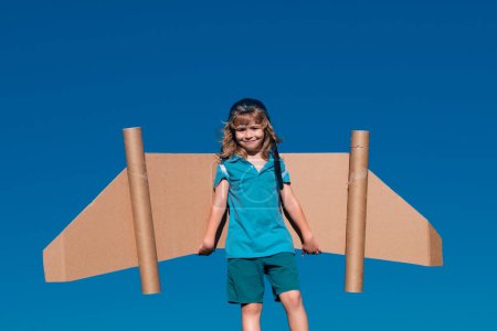 Photo for Child boy plays in an astronaut dreams of space. Happy child play with toy plane cardboard wings against blue sky. Kid having fun in summer field outdoor. Portrait of boy with paper wings - Royalty Free Image