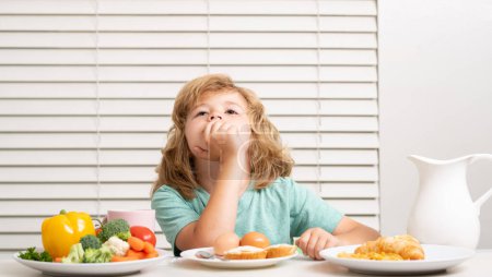 Photo for Funny blonde little boy having breakfast. Milk, vegetables and fruits healthy food nutrition for children - Royalty Free Image