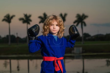 Photo for Kid boy practicing martial arts outdoor. Sport martial arts kids. Little boy wearing kimono doing karate in park. Child with boxing gloves training martial arts. Little fighter. Martial arts for kids - Royalty Free Image