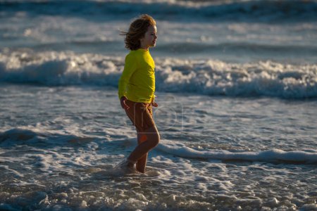 Foto de Niño corriendo en la playa divirtiéndose en las vacaciones de verano. Niños felices jugando en el mar. Niños en la naturaleza con el mar. Niños felices de vacaciones en la playa corriendo en agua de mar. Niño caminando en la playa del mar - Imagen libre de derechos