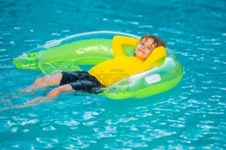 Téléchargez les photos : Heureux enfant profitant de vacances d'été en plein air dans l'eau dans la piscine. Mignon petit enfant en maillot de bain relaxant sur un anneau gonflable. Enfant flottant dans une piscine - en image libre de droit