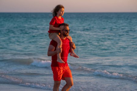 Photo for Father and son boy walking on beach. Summer holiday. Father and son enjoying summer vacation together. Son on fathers shoulders piggyback ride. Father and son spending time at sea - Royalty Free Image