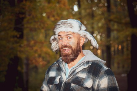 Téléchargez les photos : Passionné homme barbe expressif impulsif dans le froid glacial de l'automne gèle dans un village, portant un chapeau avec un rabat d'oreille. Capturer d'étranges idées expressives - en image libre de droit