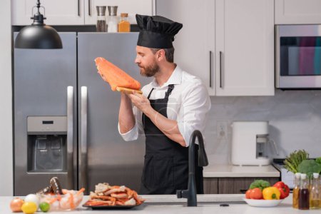 Photo for Portrait of man in chef apron and cook hat preparing fresh natural meal salmon at kitchen. Handsome cheerful chef man preparing raw fish salmon. Healthy food, cooking concept - Royalty Free Image