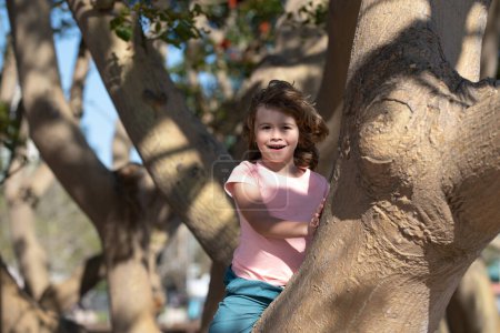 Photo for Young child climbing tree. Happy child playing in the garden climbing on the tree - Royalty Free Image