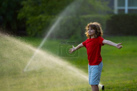 Téléchargez les photos : Mignon petit enfant jouer dans le jardin le jour d'été. Enfant profiter de l'été dans la cour arrière. Petit garçon s'amusant à courir sous arroseur pulvérisateur d'eau. Arroser l'herbe d'été. Vacances d'été pour les enfants - en image libre de droit