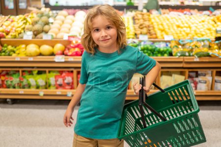 Foto de Niños con cesta de la compra. El niño está eligiendo verduras y frutas frescas en la tienda. Niño comprando comida en supermercado de comestibles - Imagen libre de derechos