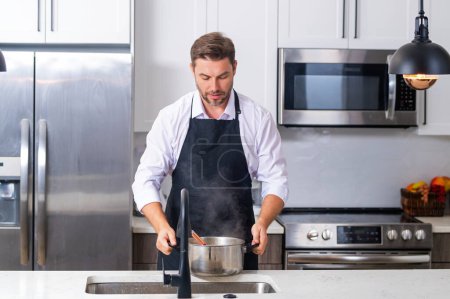 Photo for Cooking food at home. Man in kitchen preparing a meal. Male cook preparing food in kitchen at home. Chef cooking meal. Man cooking food, kitchen pot, food plate. Man preparing soup on kitchen interior - Royalty Free Image