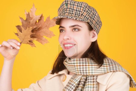 Photo for Hipster young woman in trendy autumn fall outfit stylish hat and scarf. Beauty girl hold autumn leaves near face, isolated on studio background. Portrait of autumnal woman with maple leaf - Royalty Free Image