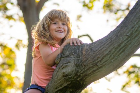 Téléchargez les photos : Garçon de 8 ans grimpant haut arbre dans le parc. Surmonter la peur des hauteurs. Bonne enfance. Enfant essayant de grimper sur l'arbre - en image libre de droit