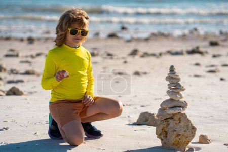 Photo for Child with zen stones on sea beach, meditation, spa and harmony. Calm balance concept. Kids play on the beach. Keep calm. Calming child and stone tower against sea. Zen Stones on beach for meditation - Royalty Free Image
