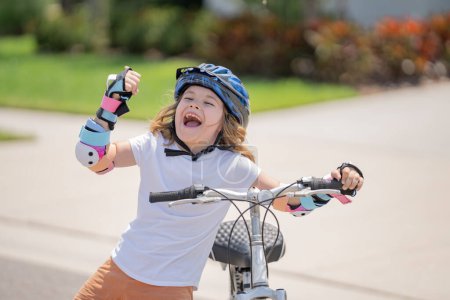 Téléchargez les photos : Joli gosse en vélo dans un parc d'été. Les enfants apprennent à conduire un vélo sur une allée à l'extérieur. Enfant à vélo dans la ville portant des casques comme équipement de protection. Enfant à vélo, vélo en plein air - en image libre de droit