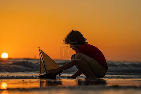 Photo for Child playing with a toy boat. Little kid boy sailing toy ship on sea water. Summer vacation with kids. Kid dreaming about sailing. Adventure and travel with children - Royalty Free Image