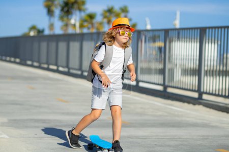Foto de Un chico patinando en patineta. Paseo de skate infantil en monopatín en el parque. Joven adolescente sonriente montando en un moderno monopatín crucero, fondo urbano - Imagen libre de derechos