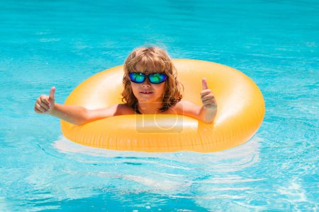 Téléchargez les photos : Enfant en lunettes de soleil flottant dans la piscine. Enfant nageant dans la piscine. Vacances d'été. Enfant heureux jouant avec anneau de natation coloré dans la piscine le jour de l'été. Jouets aquatiques pour enfants - en image libre de droit