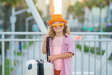 Foto de Retrato de niño moderno sonriente con equipaje, maletas de vacaciones. Los niños viajan estilo. Sueños de viaje, aventura, vacaciones. Niños viaje y viaje fin de semana - Imagen libre de derechos