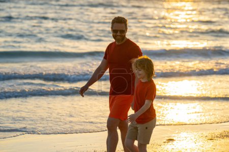 Photo for Father and son holding hands walking on sunset beach. Father and son walk in sea beach. Concept of friendly family. Happy family on beach, summer holiday vacation. Dad with kid enjoy sea - Royalty Free Image