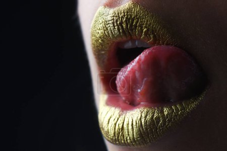 Foto de Lamiendo labios sexy lengua. Estilo brillante para un labio sexy. Labios de mujer sensuales. Boca dorada de lujo. Labios dorados glamour. Labios dorados con pintura dorada o lápiz labial metálico - Imagen libre de derechos