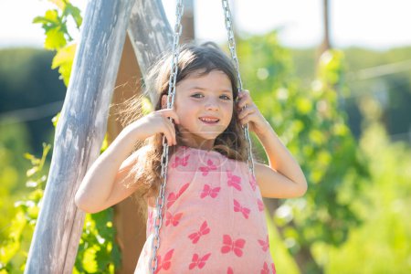 Photo for Child playing on swing. Healthy summer activity for children in warm weather. Little kids swinging. Cute little girl having fun on a swing in beautiful summer garden and sunny day outdoors - Royalty Free Image