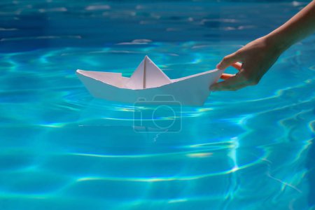 Foto de Barco de papel navegando en el agua causando olas y ondulaciones. Mano poniendo un barco de papel en el agua. Origami barco de papel - Imagen libre de derechos