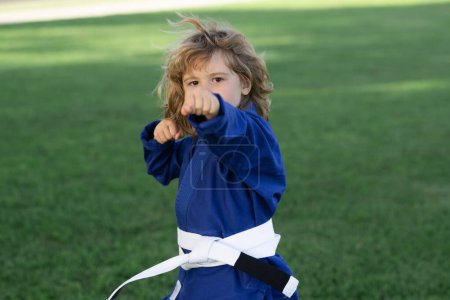Foto de Niño practicando karate al aire libre. Niños de karate deportivo. Un niño usando kimono haciendo karate en el parque. Pequeño luchador de karate. Artes marciales para niños. Deporte, acción, deportes de combate - Imagen libre de derechos