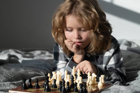 Photo for Child playing chess on bed. Clever child thinking about chess. Portrait of clever kid with chessboard. Boy play chess - Royalty Free Image