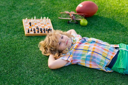 Photo for Chess game for children. Kid relax in park, laying on grass, daydreaming. Kid playing chess. Games and activities for children - Royalty Free Image