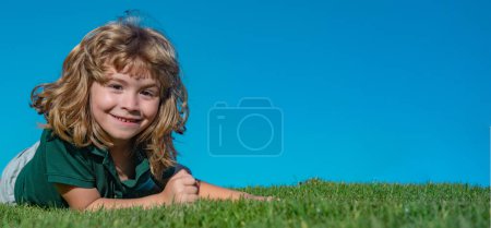 Téléchargez les photos : Enfant garçon se détendre à l'extérieur dans la journée ensoleillée d'été. Joyeux enfant étendu sur l'herbe verte. Enfant drôle en plein air dans le jardin de printemps. Printemps et enfant. Grande bannière photo pour en-tête de site Web - en image libre de droit