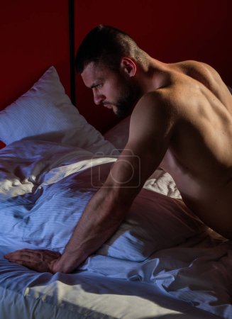 Foto de Sexy and naked muscular young man posing on the sofa. Sexy shirtless male model lying in bed. Attractive young naked man lying in bed. Romantic dreaming nude male model with booty buttocks in bed - Imagen libre de derechos
