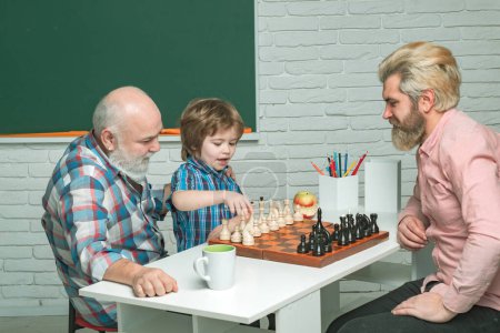 Photo for Grandfather father and son playing chess, men in different ages ready to study. Happy family in class at school. Three men generation. Senior teacher - Royalty Free Image