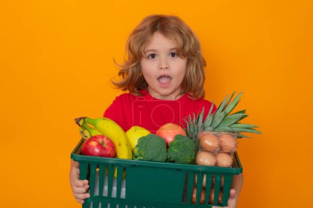 Photo for Shopping grocery. Cute child hold shopping cart full of groceries. Kid holds shopping basket over yellow background. Store, shopping, sales and discounts - Royalty Free Image