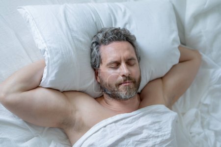 Téléchargez les photos : Tête d'homme sur oreiller. Homme aux cheveux gris dormir dans un lit blanc. Un aîné dort au lit dans sa chambre. L'homme mûr dort à la maison le matin. Bon sommeil. Homme millénaire dormant au lit. Les gens dorment, dorment - en image libre de droit