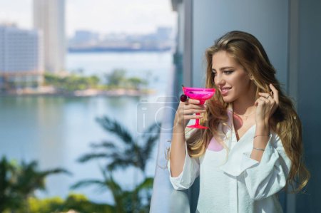 Foto de Hermosa mujer rubia sexy disfrutar de cóctel de bebida en la terraza balcón en las vacaciones de verano. Elegante mujer bebiendo cóctel en un hogar. Hermosa chica bebiendo cóctel. fin de semana de vacaciones de verano en el hotel - Imagen libre de derechos