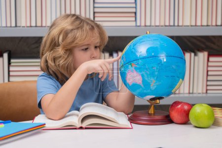 Photo for Pupil looking at globe in library at the elementary school. Nerd school kid. Clever child from elementary school with book. Smart genius intelligence kid ready to learn. World globe - Royalty Free Image