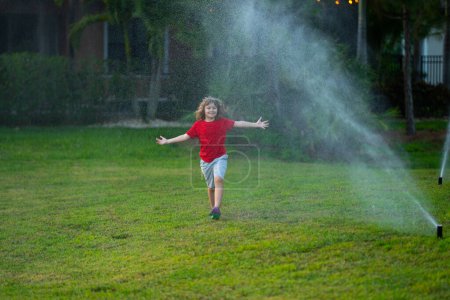 Téléchargez les photos : Enfant jouant dans la cour d'été. Amusement aquatique dans le jardin. Jeu d'enfant avec arroseur d'eau dans le jardin. Petit garçon drôle jouant avec tuyau d'arrosage de jardin dans la cour. Enfant s'amuser avec de l'eau pulvérisée - en image libre de droit