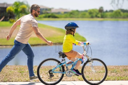 Photo for Father and son learning to ride a bicycle having fun together at Fathers day. Father teaching his son cycling on bike in american neighborhood. Father and son concept. Father support son - Royalty Free Image