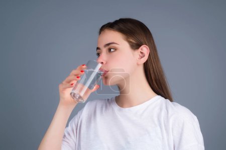 Photo for Young woman drinking a fresh glass of water, isolated on studio background. Thirsty woman holding glass drinks still water preventing dehydration, water balance, healthy lifestyle - Royalty Free Image