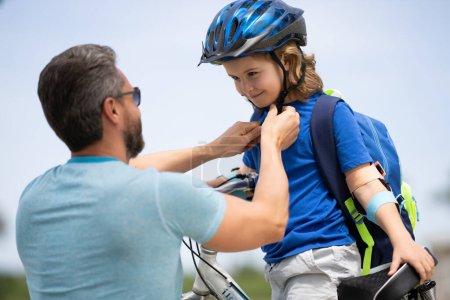 Photo for Insurance child. Father teaching son cycling on bike. Father learn little son to ride a bicycle. Father support and helping son. Fathers day concept. Father helping his son to wear a cycling helmet - Royalty Free Image