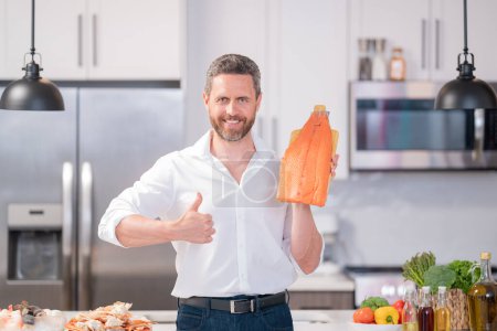 Foto de El hombre hispano milenario sostiene el filete de salmón en la cocina. Cocinar filete de salmón. Menú restaurante con filete de salmón. Cocinar, publicitar el concepto de filete de salmón - Imagen libre de derechos