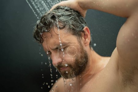 Foto de Hombre de mediana edad lavando el cabello en el baño. Cabezal de ducha en la bañera. Cara en espuma en la ducha. Bañista duchándose. Un tipo cercano duchándose. Concepto ducha. El hombre está bajo las gotas de agua en las duchas - Imagen libre de derechos
