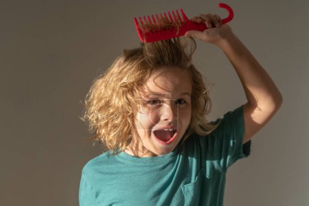 Photo for Comb and hair brush concept. Kid boy makes face expressions, combing hair. Child with tangled blonde long hair tries to comb it. Hair portrait kid with a comb - Royalty Free Image