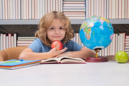 Photo for School boy with books and apple in library. Cute pupil looking at globe in library at the elementary school. School child. Kid boy from elementary school. Pupil go study. Clever schoolboy learning - Royalty Free Image