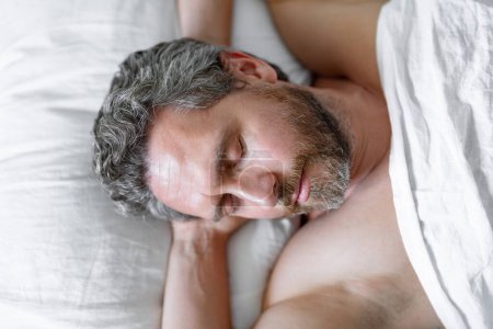 Foto de El hombre duerme en la cama blanca. Hombre sexy sin camisa dormir en la cama en el dormitorio. Hombre maduro hispano duerme en casa por la mañana. Buen sueño. Hombre durmiendo en la cama. La gente se acuesta, descansa. - Imagen libre de derechos
