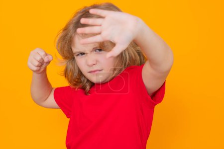 Photo for Andry child in red t-shirt making stop gesture on isolated studio background. Child with fist gesture fight. - Royalty Free Image