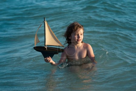 Photo for Little boy playing with toy sailing boat, toy ship. Travel and adventure concept. Child feeling adventurous while cruising. Kid on summer sunset beach. Kid playing on the beach at the sunset time - Royalty Free Image