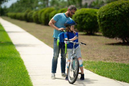 Téléchargez les photos : Concept père et fils. Père enseignant fils à vélo. Père aidant son fils à faire du vélo dans le quartier américain. Enfant en casque de sécurité apprenant à faire du vélo avec son père. Fête des pères - en image libre de droit